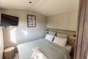 Un dormitorio con una cama, un televisor montado en la pared y un ventanal que deja entrar luz natural.