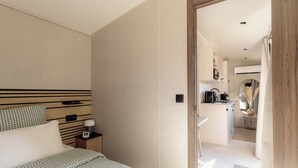 A hotel room with a bed, bedside table, lamp, and a view into the kitchen area.
