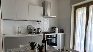 Moderni keittiö, jossa on valkoiset kaapit, kaasuliesi ja uuni. Ruokapöydällä on kaksi ruukkukasvia.