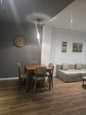 Ein modernes Wohnzimmer mit Essbereich, ausgestattet mit einem Holztisch und -stühlen, einem grauen Sofa und zwei Wandbildern.