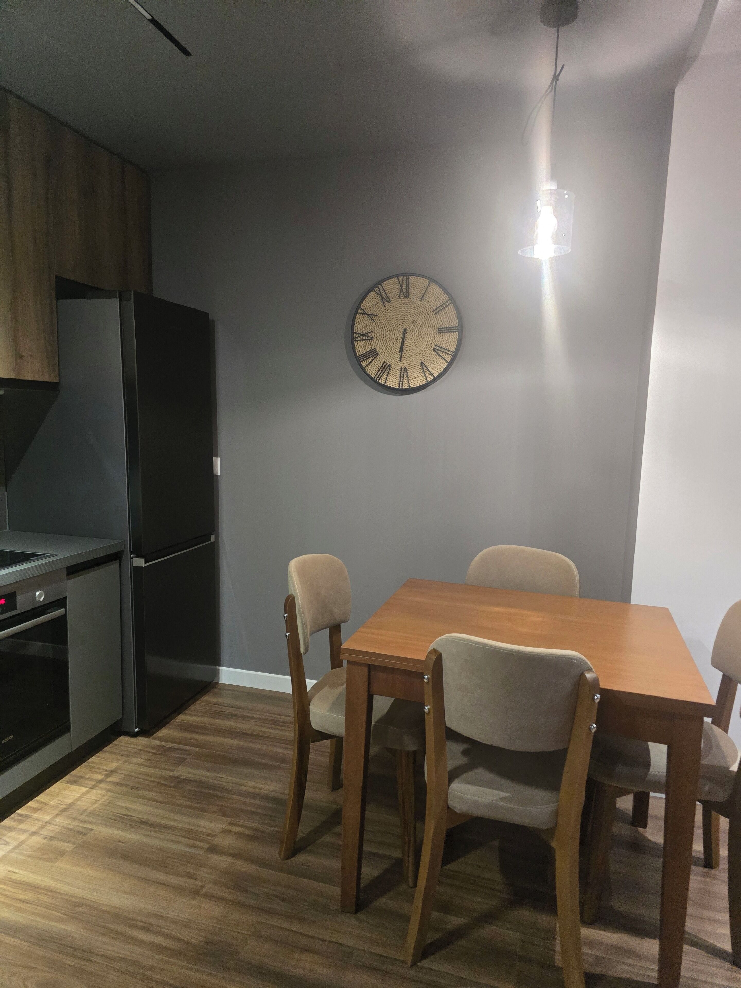 Une cuisine moderne avec une table et des chaises en bois, un four encastré et une horloge murale.