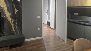 Eine moderne Küche mit grauen Schränken und einer Holzausziehtheke, ein Essbereich mit einem Holztisch und Stühlen sowie ein Flur mit einer Marmorwand und einer Tür zu einem anderen Raum.