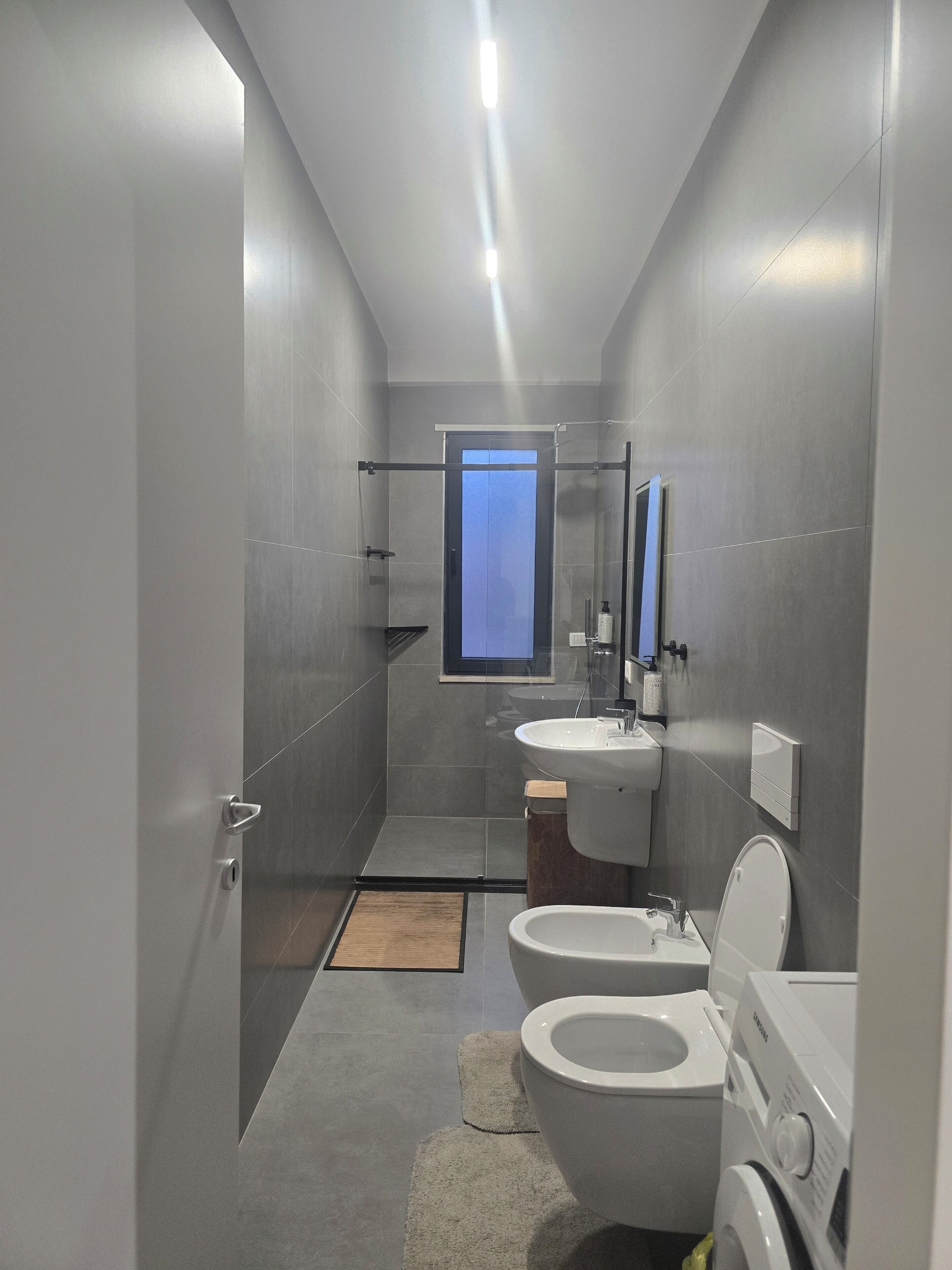 A modern bathroom with a shower, toilet, sink, and a built-in window.