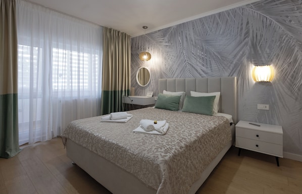 A neatly made bed with a patterned bedspread, a bedside table with a lamp, and a wall with a leaf-patterned design.