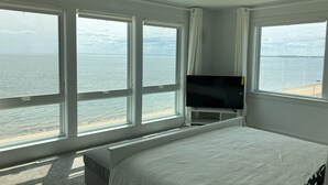 Un dormitorio con una cama grande, un televisor sobre un mueble bajo y vista al mar a través de amplias ventanas.