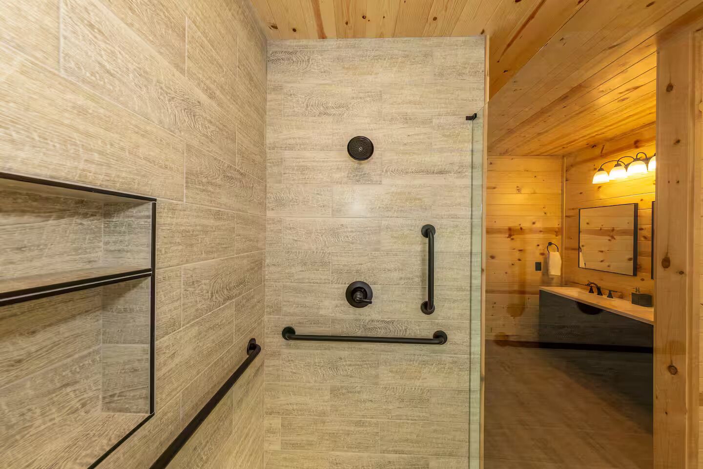 A wooden interior with a glass shower door, a wooden bench, and a bathroom with a sink and mirror.