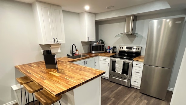 A modern kitchen with white cabinets, a wooden island, stainless steel appliances, and a bar stool.