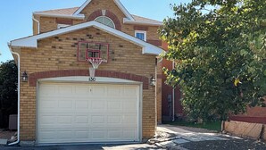 A two-story house with a garage door, a basketball hoop, and a tree in front.