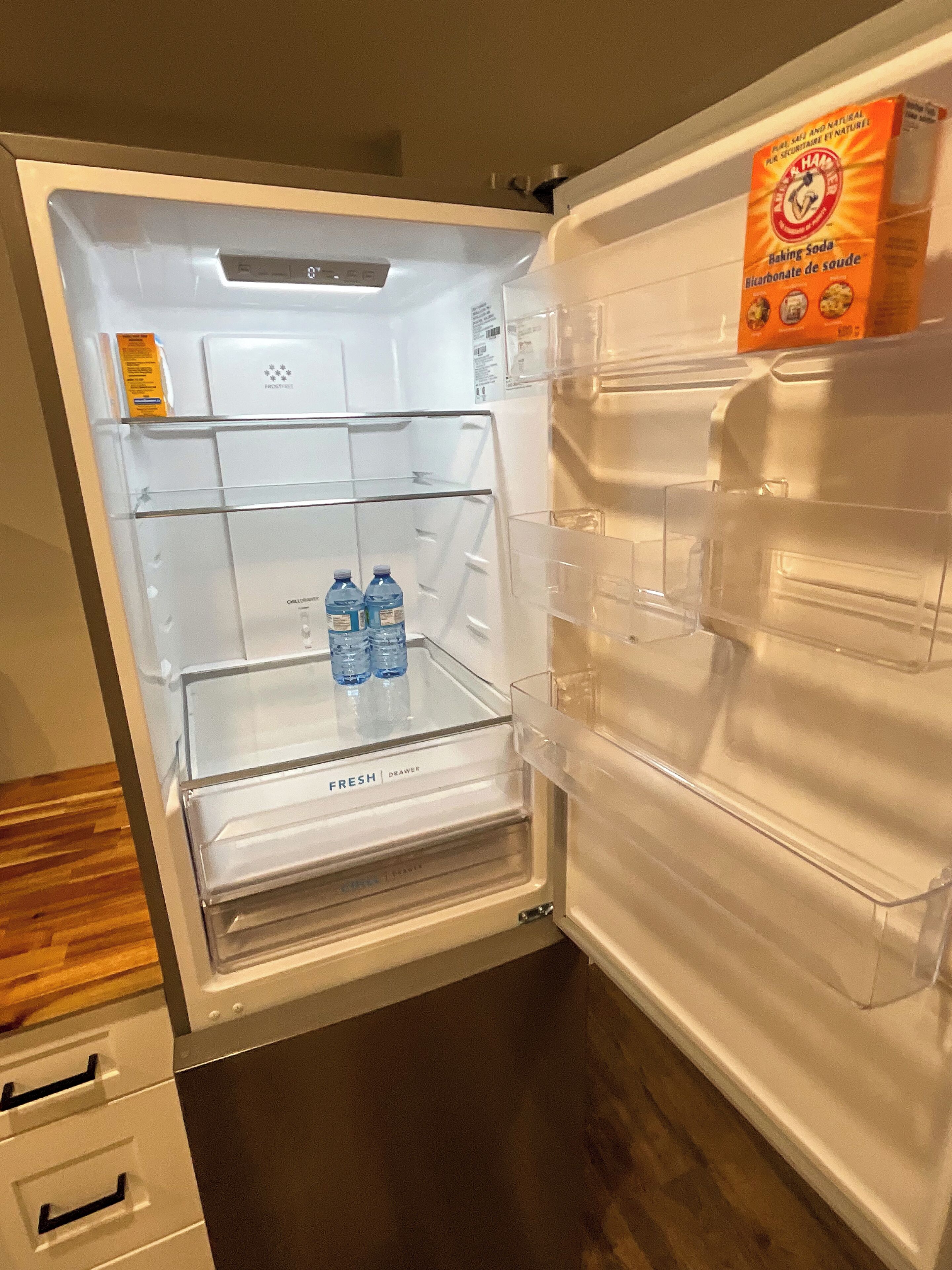 An open refrigerator with a fresh drawer, two bottles of water, and a box of baking soda on the door shelf.