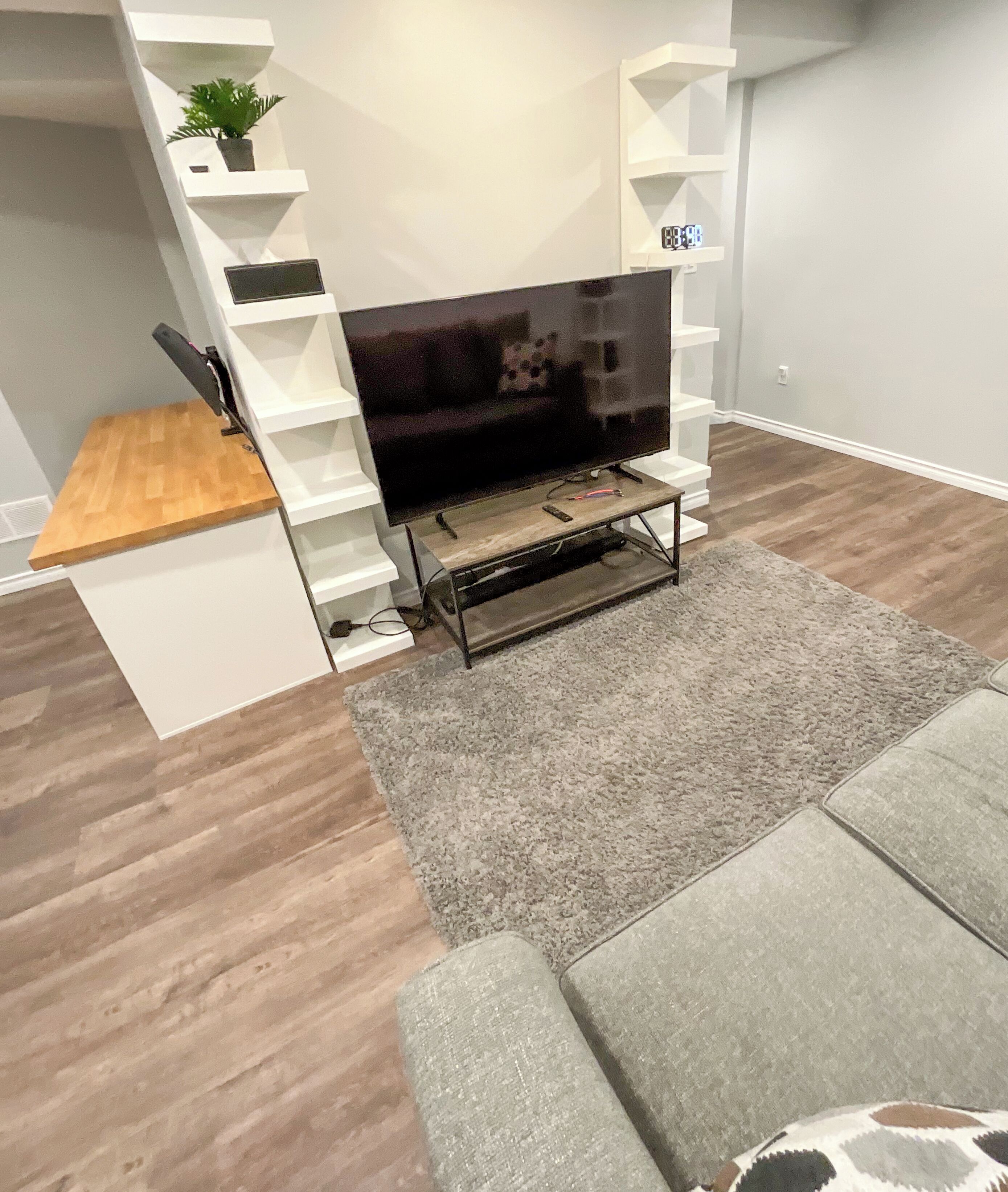 A modern living room with a flat-screen TV on a wooden stand, grey carpet, and a grey sofa.