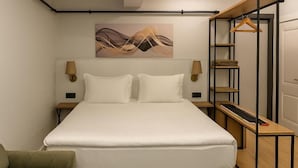A neatly arranged hotel room with a bed, a side table, a chair, and a wall-mounted shelf with a hanging garment. - Sare Apartment Sultanahmet (Istanbul)