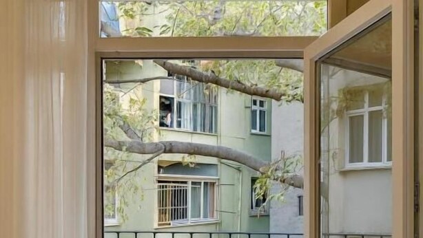 A view through a door with a patterned floor, leading to a balcony with a view of a multi-story building and a tree. - Sare Apartment Sultanahmet (Istanbul)