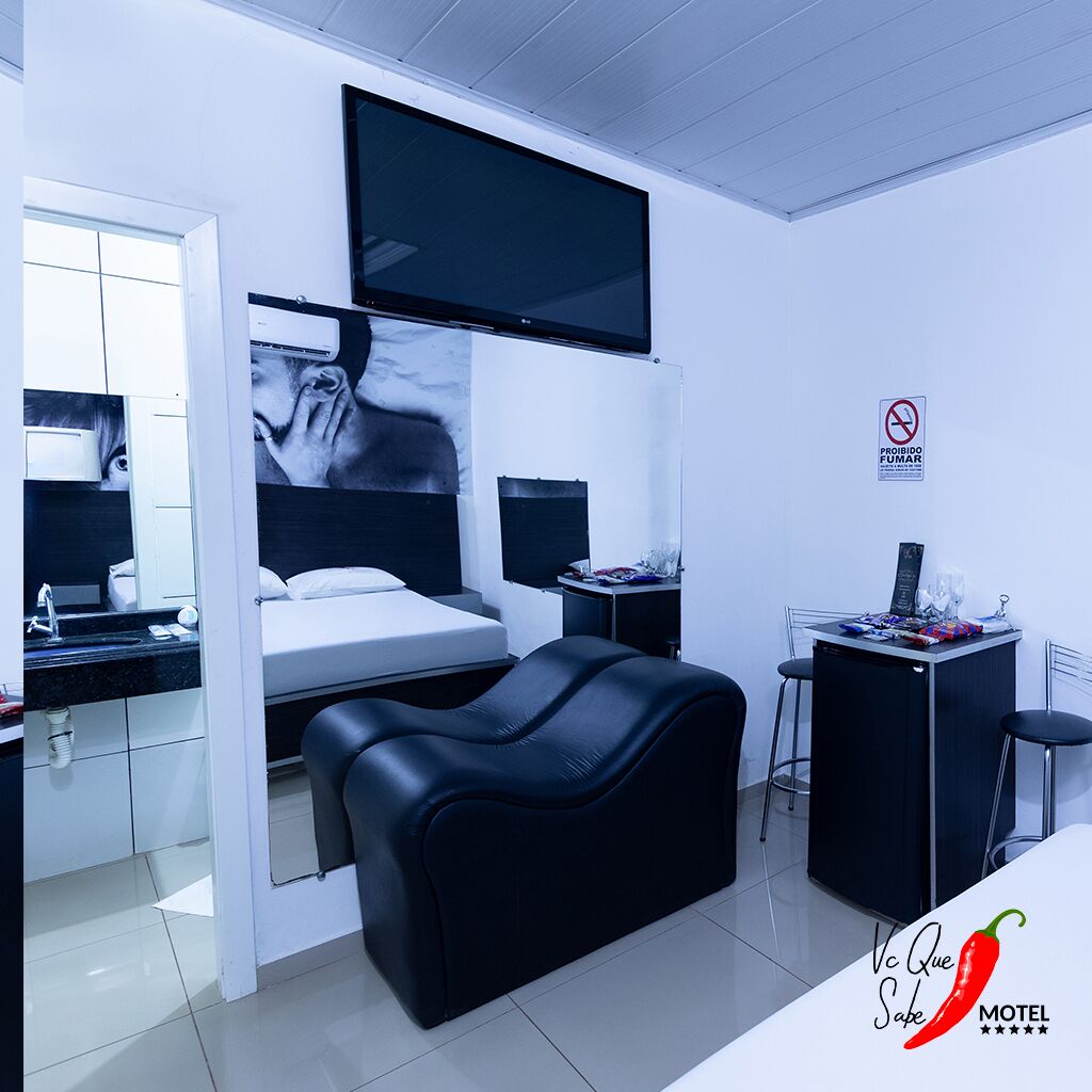 A modern hotel room with a bed, a TV, a desk with a chair, and a small kitchenette.