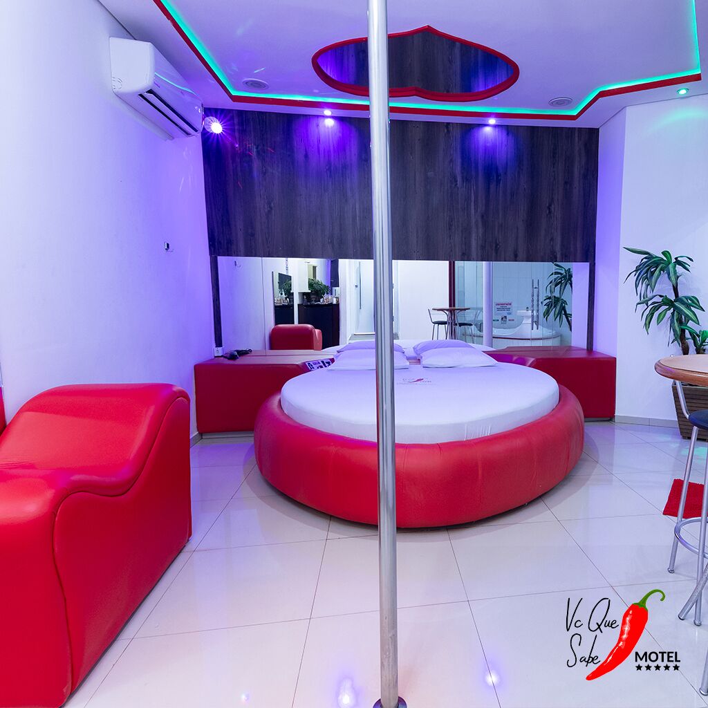 Une chambre de motel moderne avec un lit rond, des sièges rouges et une grande fenêtre.
