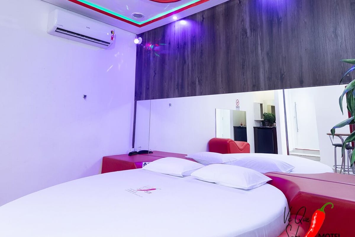 Una habitación de hotel moderna con cama, una pared de acento roja, un espejo grande e iluminación roja y verde en el techo.