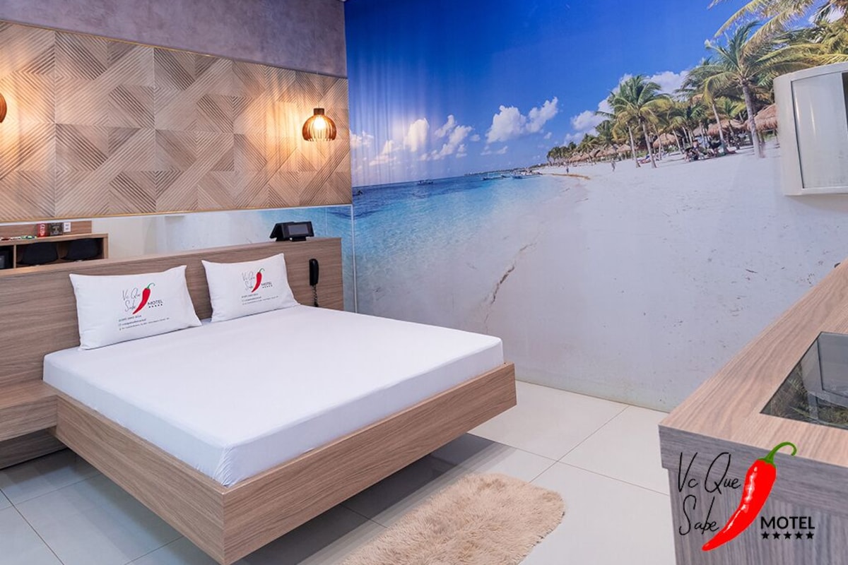 Un dormitorio moderno con una cama, un televisor montado en la pared y un mural con motivos playeros.