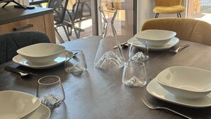Een eettafel gedekt met witte kommen, borden en bestek, en een glazen vaas met een bergmotief.