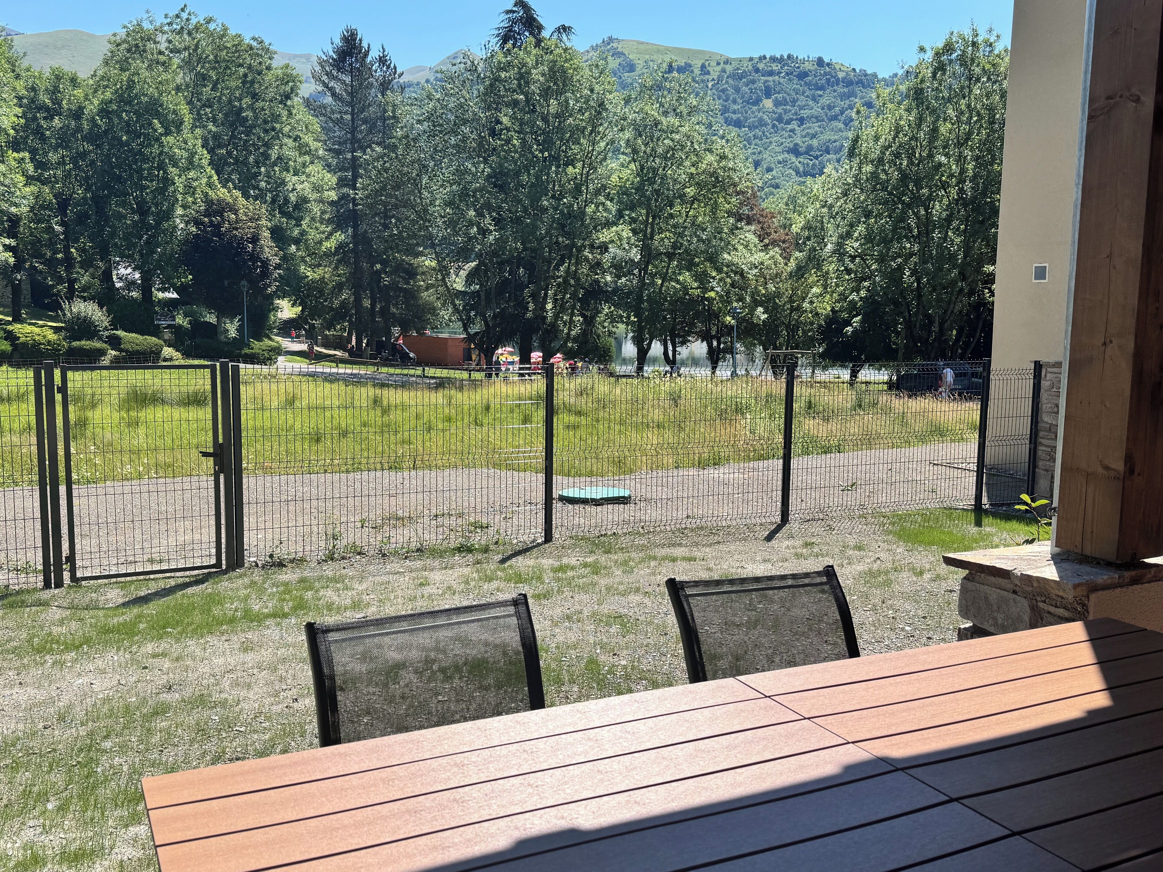 A patio with a table and chairs, overlooking a fenced area with a playground.
