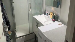 Un baño pequeño con cabina de ducha de vidrio, un lavabo blanco, un espejo y una lavadora.