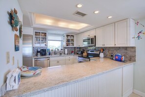 A modern kitchen with white cabinetry, stainless steel appliances, and a granite countertop. - Salt Life – 2Bed/2Bath Beachfront Condo with Pool & Elevator Access (Marathon)