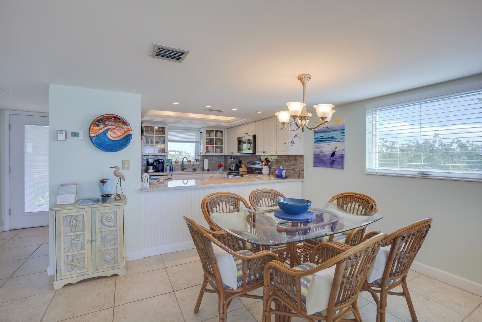 A modern kitchen with white cabinets, a dining area with wicker chairs, and a view of the ocean through the window.