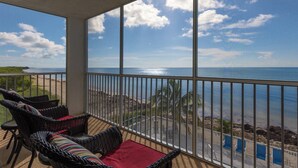 Un balcon avec des fauteuils en osier et un coussin rouge, donnant sur une plage et l’océan.
