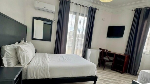 Une chambre d’hôtel avec un lit, un bureau, une chaise, une télévision et une fenêtre avec des rideaux.