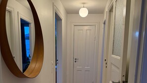 Un corridoio con pavimento in legno, pareti bianche, uno specchio rotondo e una porta con vetri satinati.