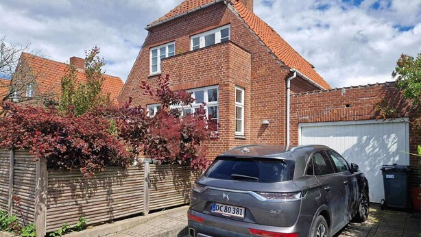 Un'auto nera parcheggiata in un vialetto, con una casa in mattoni sullo sfondo.