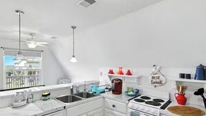 Una cucina moderna con mobili bianchi, un piano cottura e un lavello. Sono presenti delle ventole a soffitto e una finestra che permette l'ingresso di luce naturale.