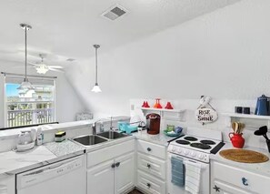 Eine moderne Küche mit weißen Schränken, einem Herd und einer Spüle. Deckenventilatoren und ein Fenster sorgen für natürliches Licht.