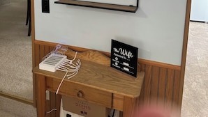 Una habitación con ventilador de techo, un espejo, un escritorio de madera con un cartel sobre wifi y una puerta que da a otra habitación.
