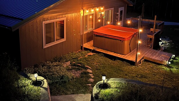 Una cabaña de madera con jacuzzi y terraza, rodeada de un paisaje boscoso.