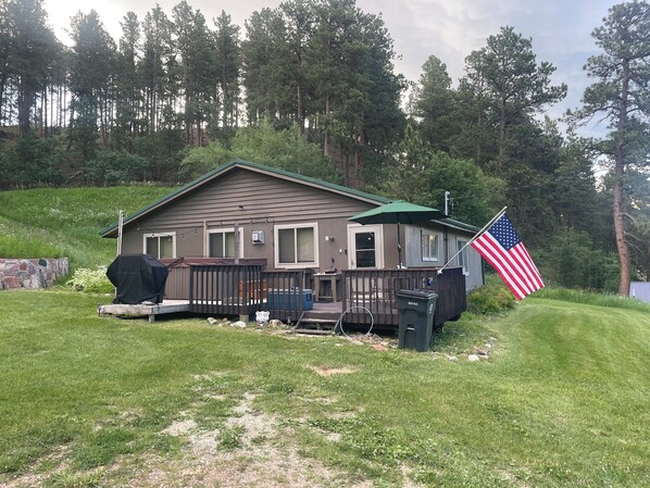 A single-story cabin with a deck, a covered grill area, and an American flag.