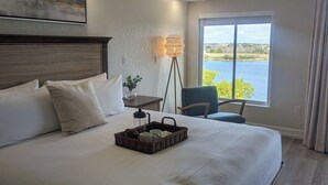 Ett hotellrum med en stor säng, en takfläkt, en sänglampa, ett fönster med utsikt över en sjö och en tavla på väggen.