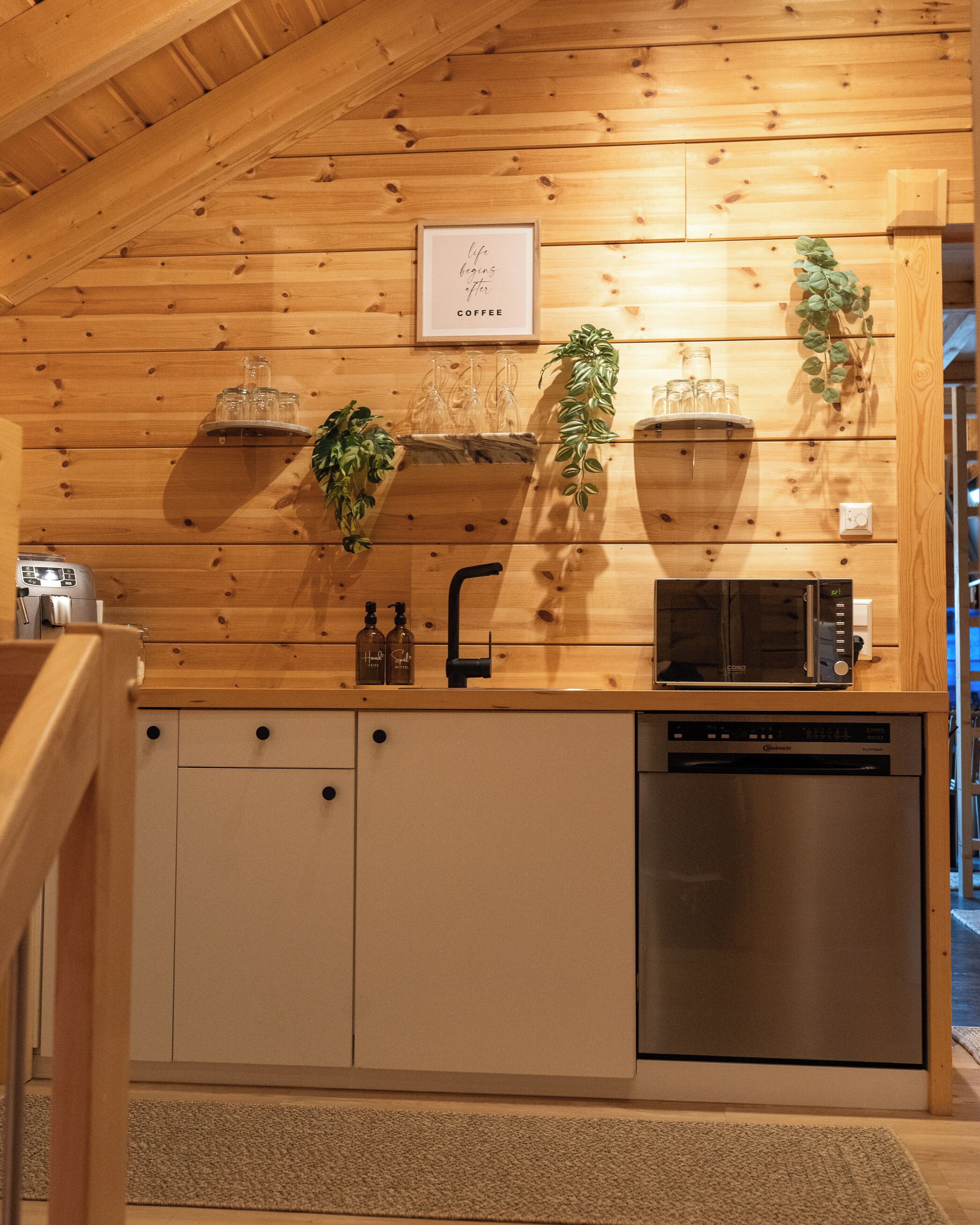 A compact kitchen with wooden walls, a built-in microwave, a dishwasher, and a sink with a faucet.