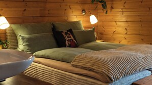 A wooden cabin bedroom with a bed, pillows, a bedside lamp, and a hanging plant. - Sohana Chalet (Kappel-Grafenhausen)