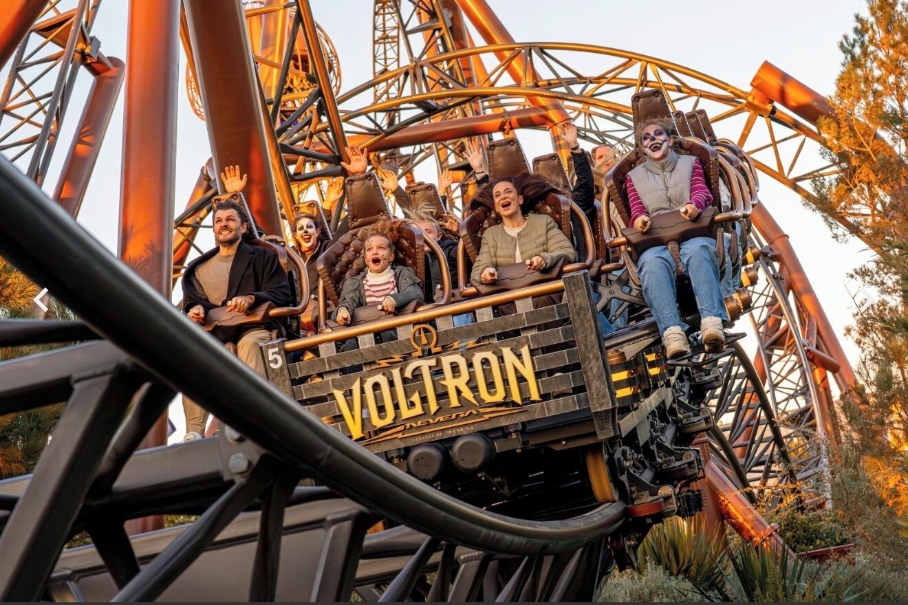 A roller coaster with the name 'Voltron' on the front, passengers seated, and a metal structure.