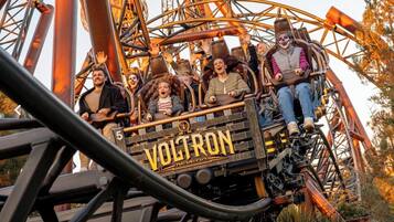 A roller coaster with the name 'Voltron' on the front, passengers seated, and a metal structure.