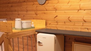A compact kitchenette with a small refrigerator, a clock on the wall, and wooden paneling. - Sohana Chalet (Kappel-Grafenhausen)