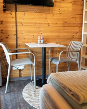 Una stanza accogliente con un muro in legno, un tavolino rotondo, due sedie e un divano.