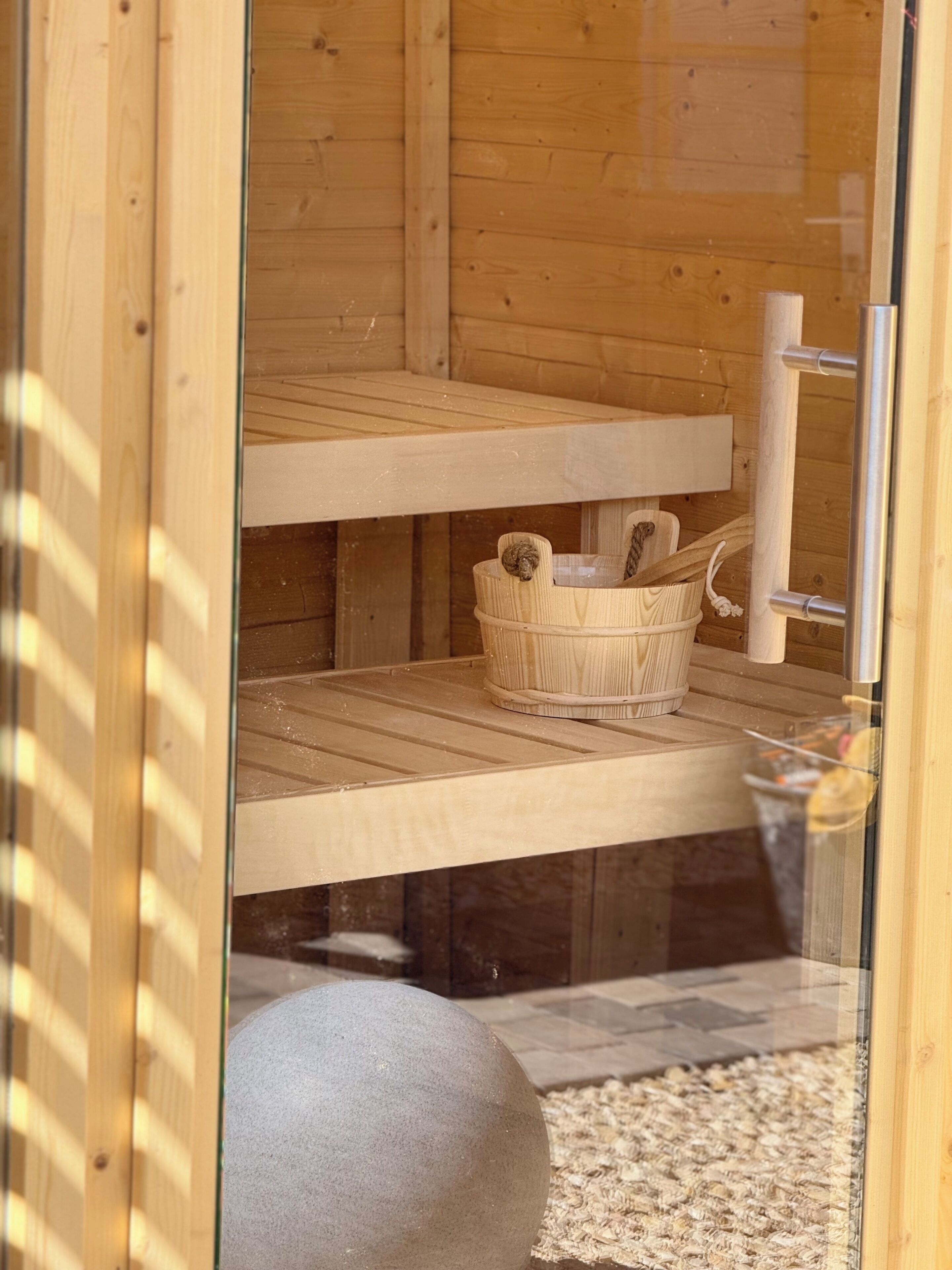A wooden sauna with a stone bench, a woven basket, and a metal towel rack.