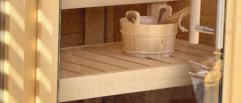 A wooden sauna with a stone bench, a woven basket, and a metal towel rack.