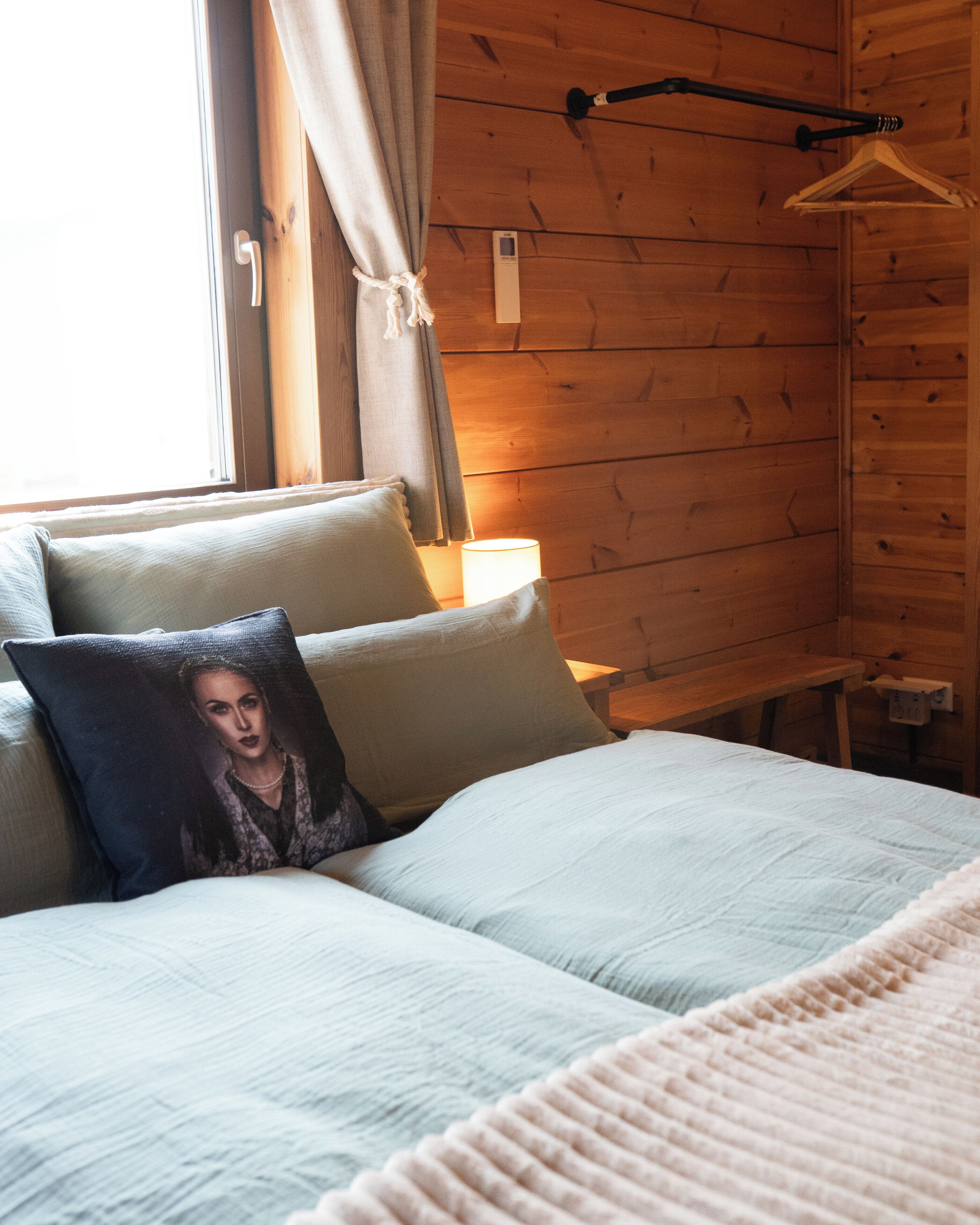 Ein Bett mit Kissen, ein Nachttisch, eine Lampe und ein Fenster mit Vorhängen.