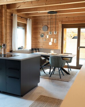 Una cocina moderna con una isla central, vigas de madera y un comedor con mesa y sillas.