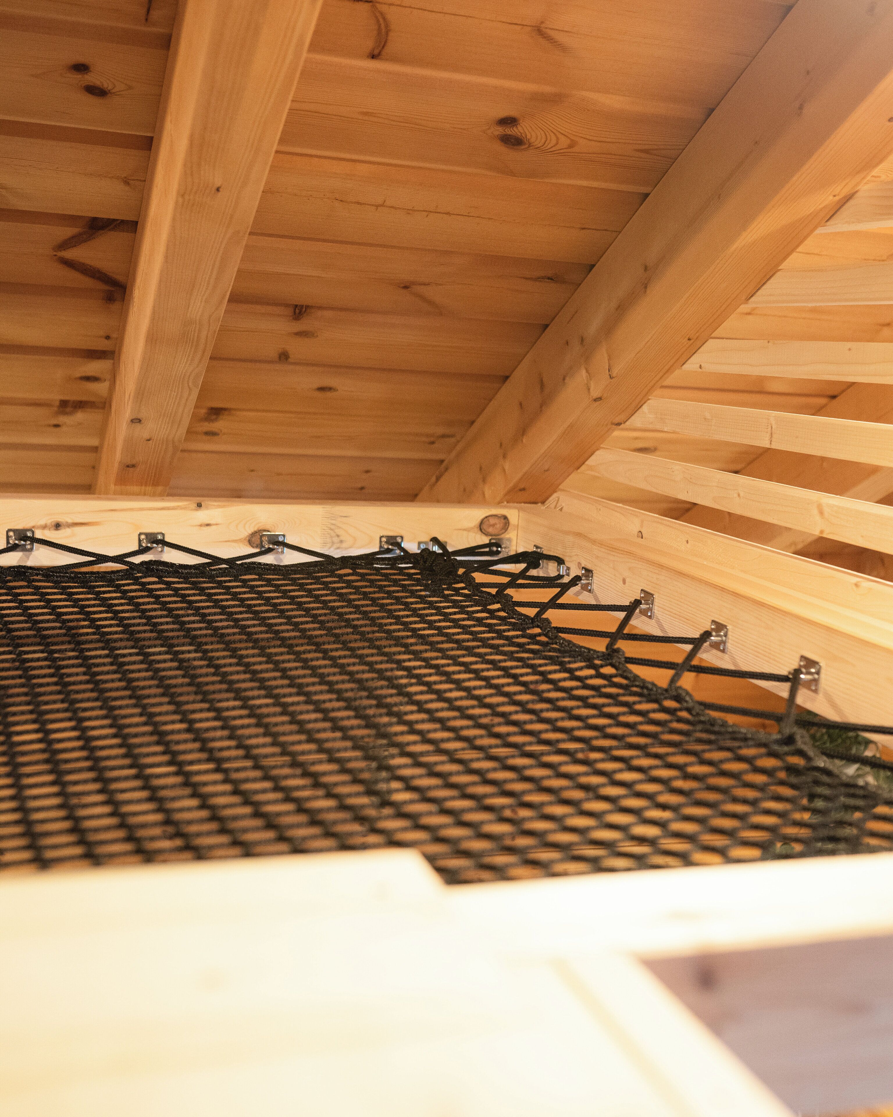 A wooden ceiling structure with visible beams and a netted floor.