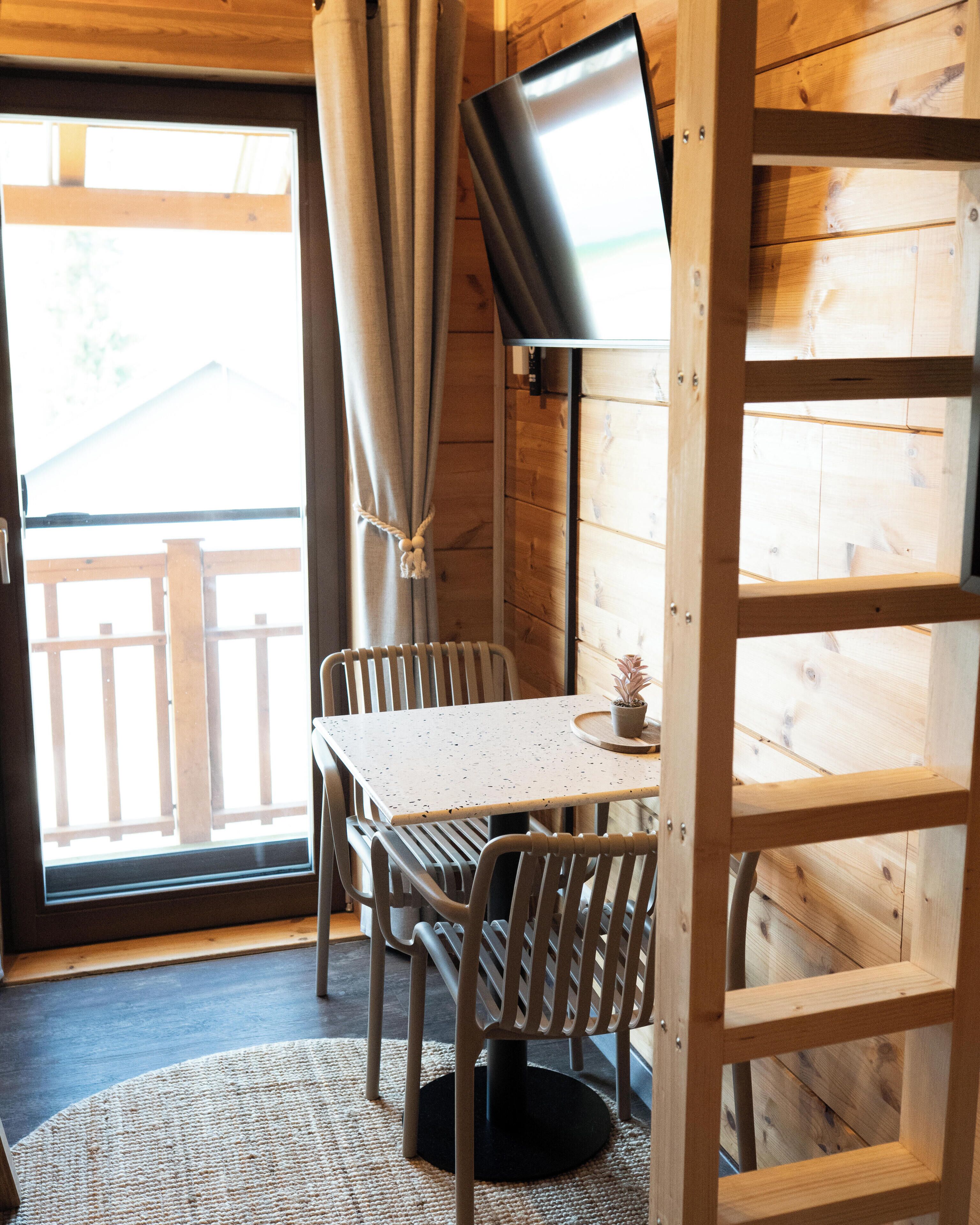 Un intérieur en bois avec une table et des chaises, un téléviseur fixé au mur et une vue à travers une porte vitrée.