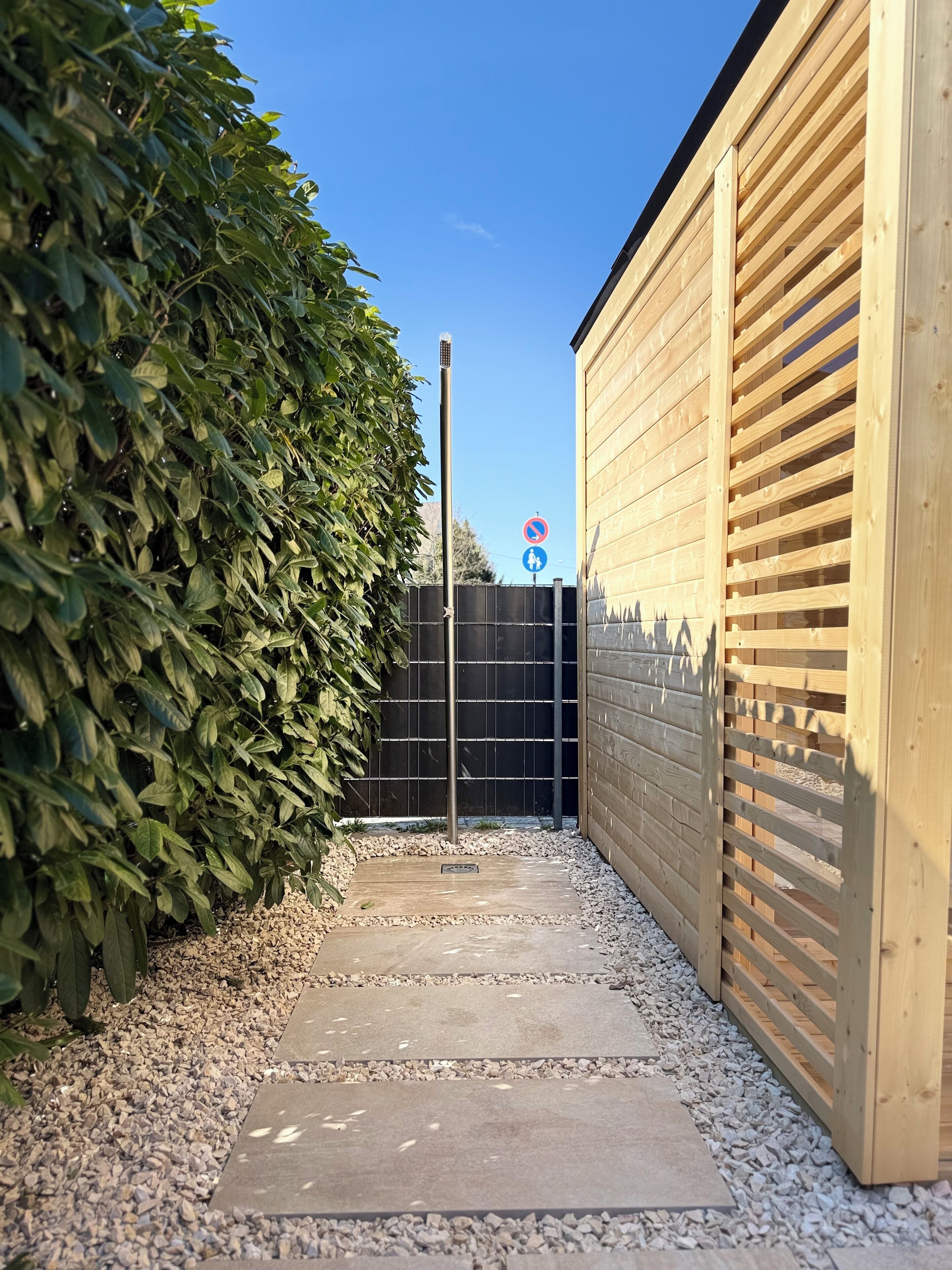 A narrow pathway leading to a wooden building with a metal gate and a no-entry sign.