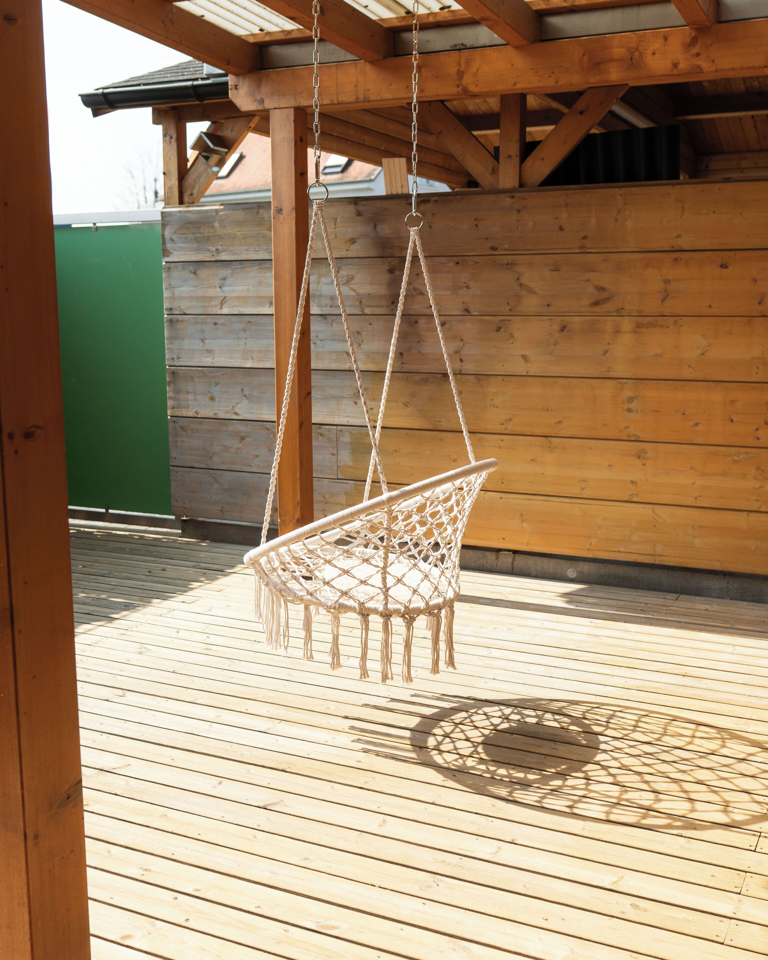 Eine Holzterrasse mit einer hängenden Schaukelstuhls.