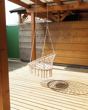 Une terrasse en bois avec un fauteuil suspendu.